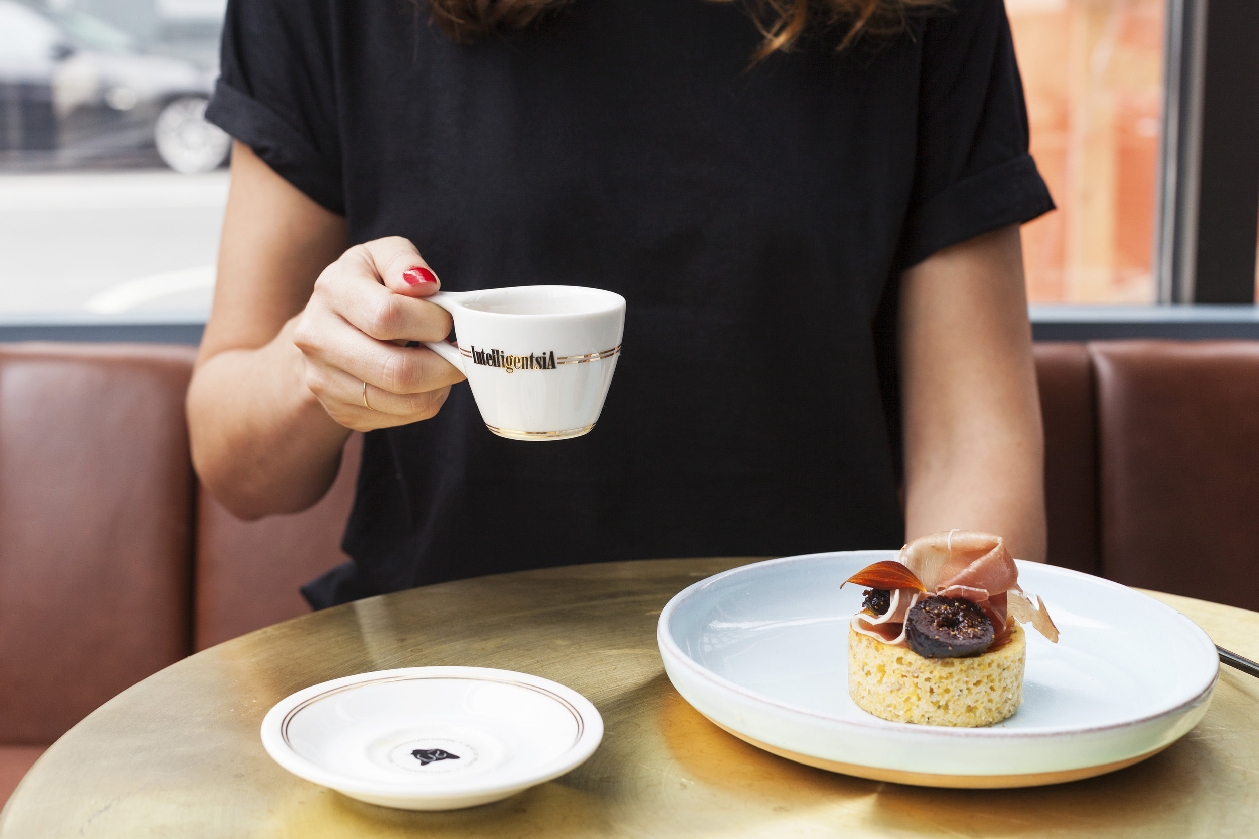 Guest holding an Intelligentsia espresso cup with a savoury fig muffin at a brass table