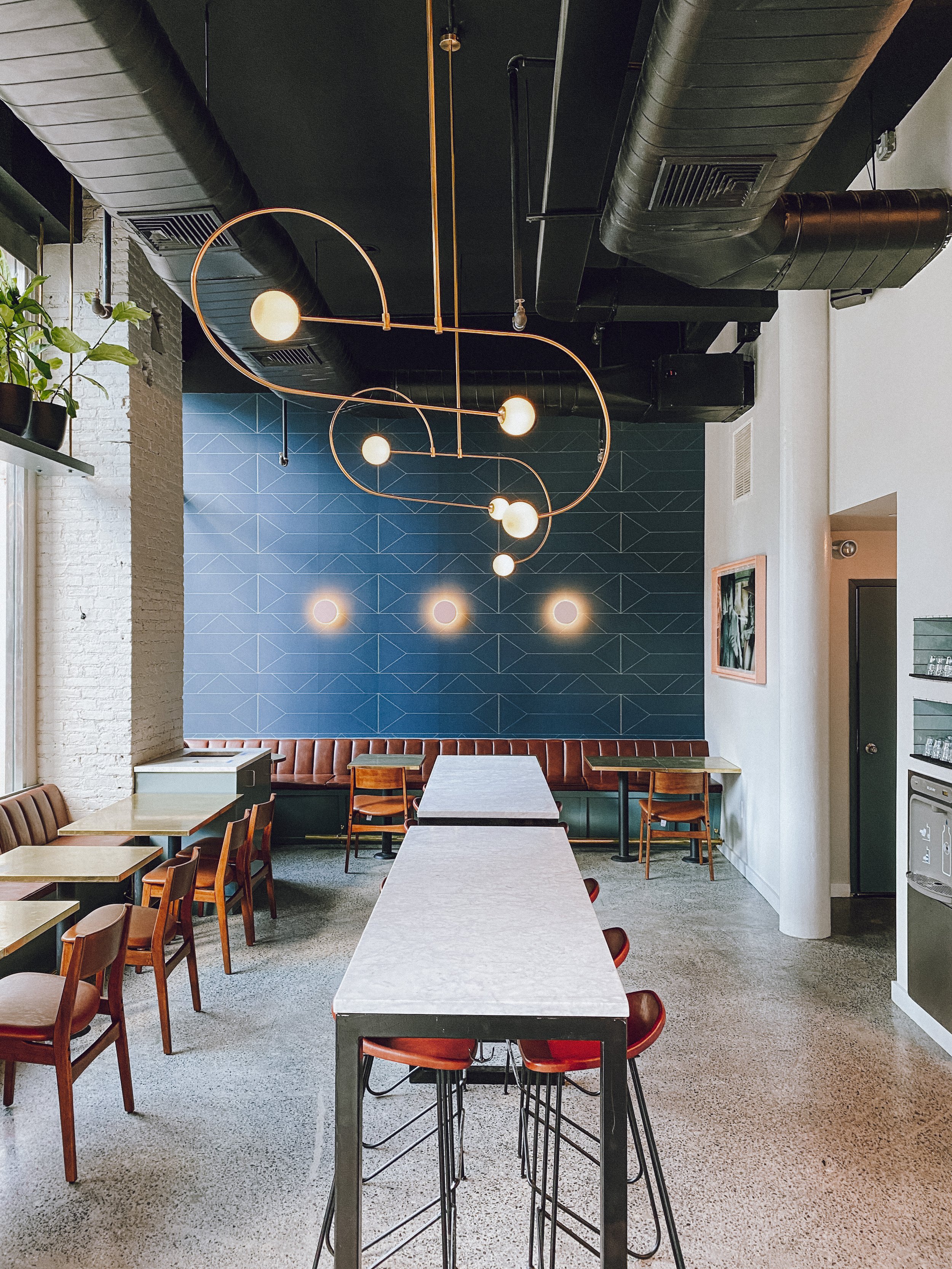 Butler dining room with a blue tiled accent wall, brass chandelier and long communal marble table