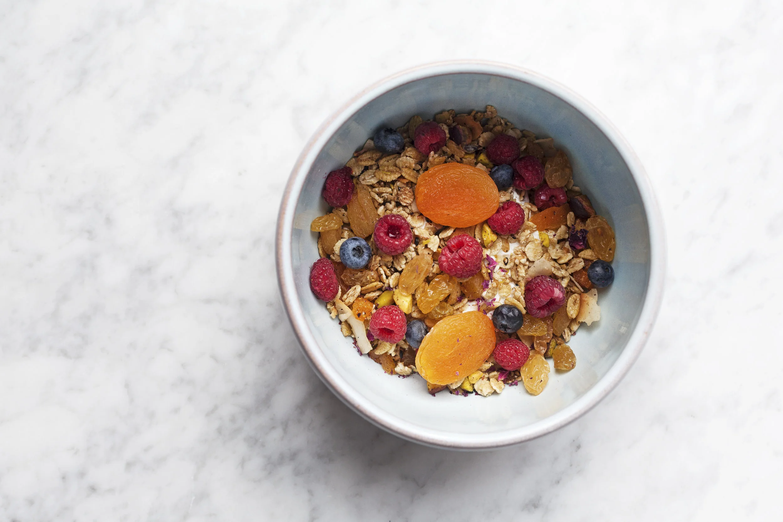 Granola parfait with raspberries, blueberries and dried apricots on white marble