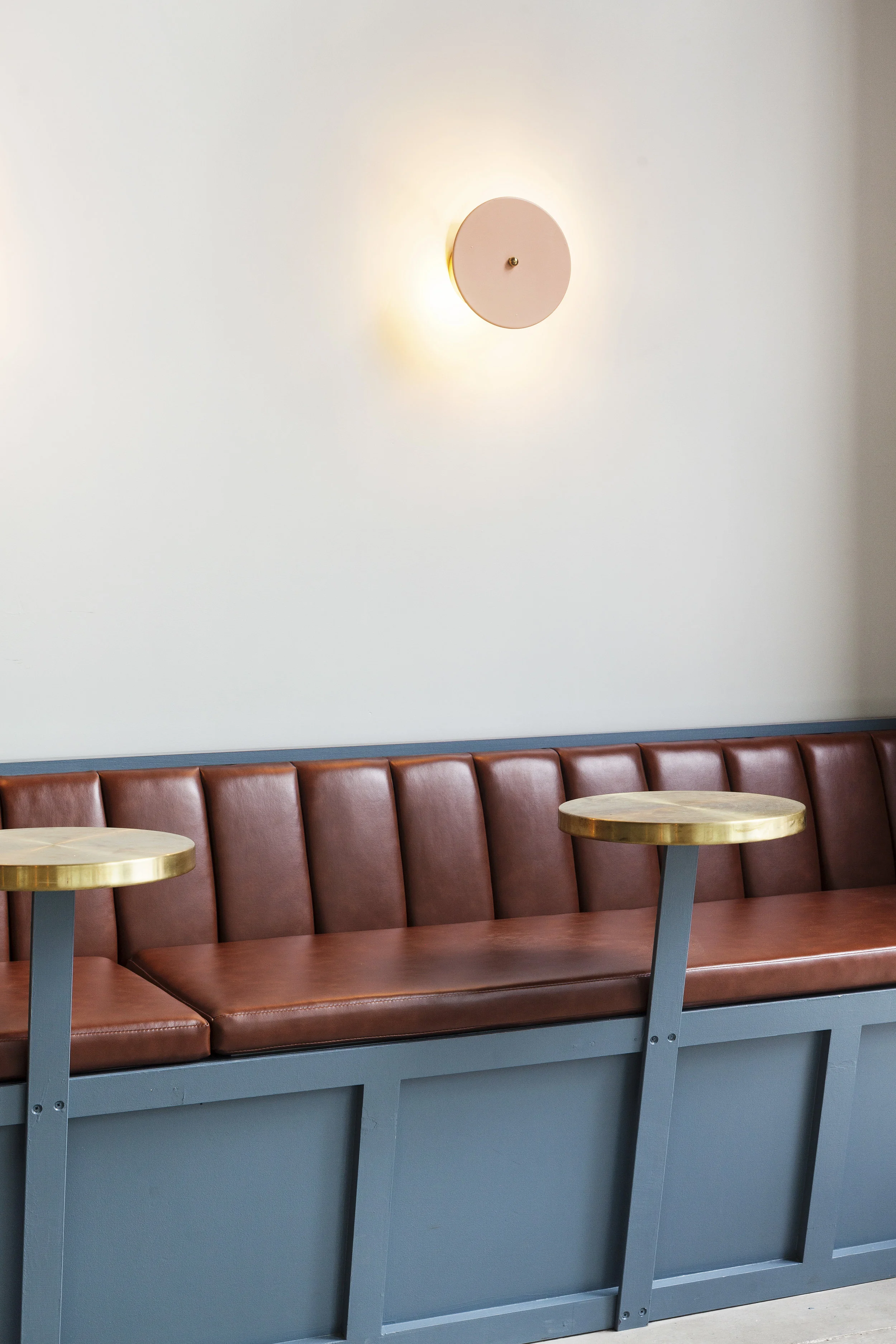 Leather banquette with brass round tables and a pink disc wall sconce