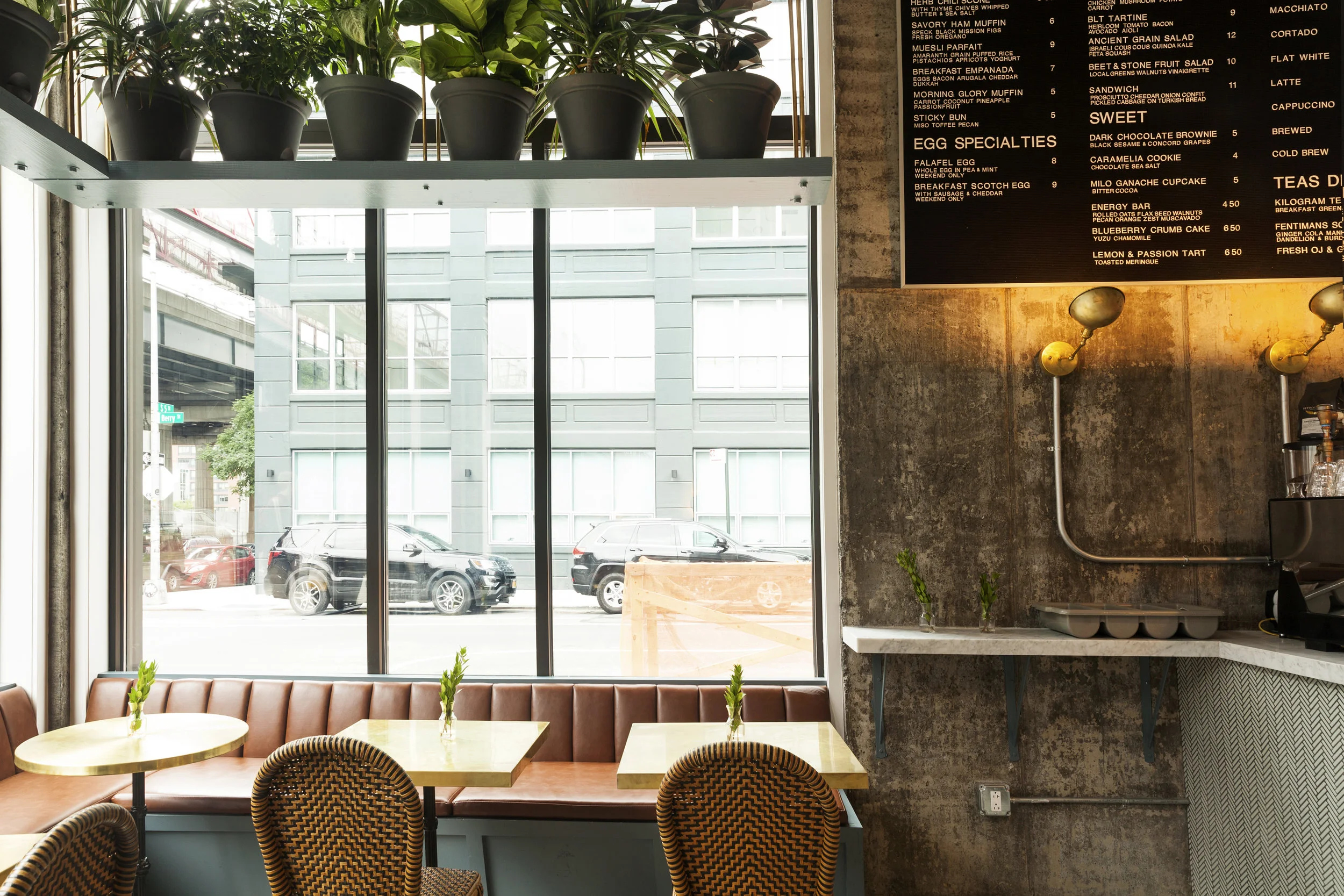 Window-side seating with a plant shelf, leather banquette, rattan chairs and brass tables