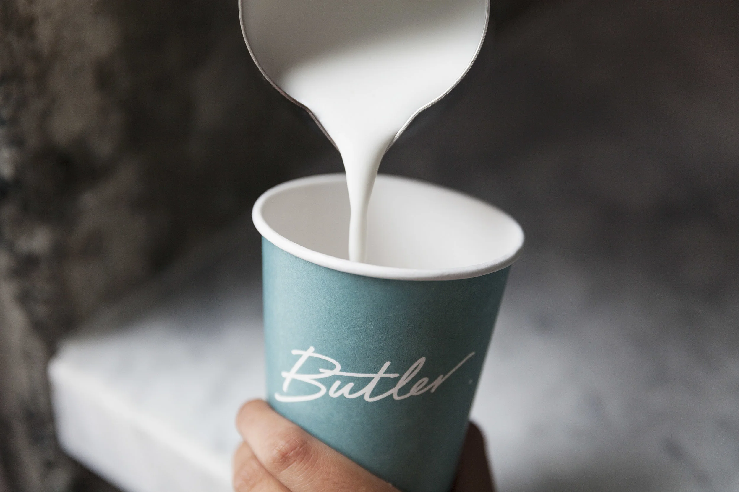 Hand holding a Butler-branded teal cup as milk begins to pour in