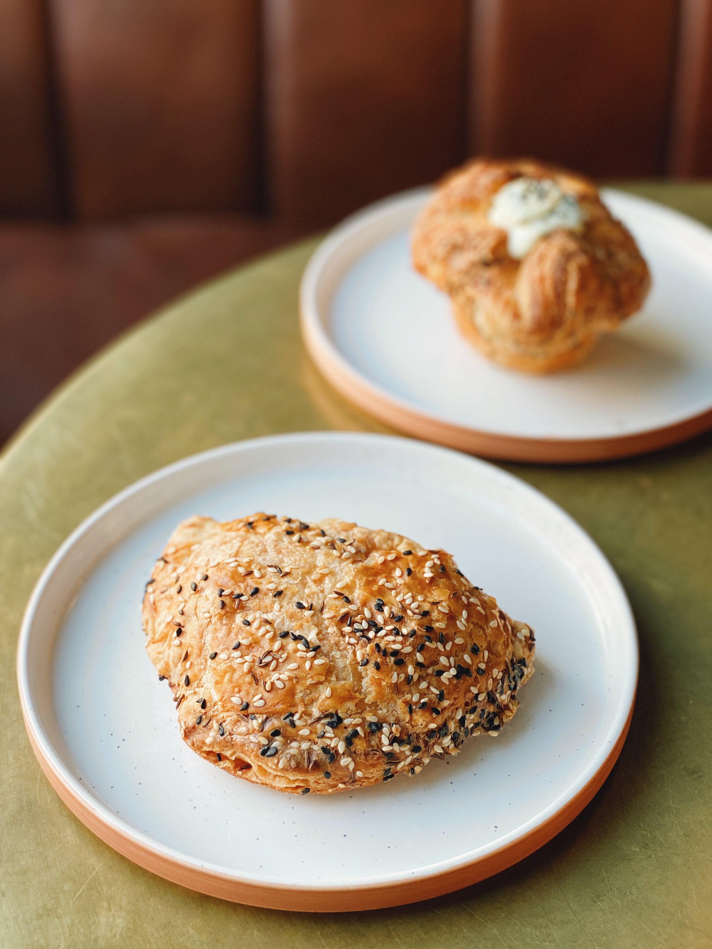 Sesame-seeded empanada and filled puff pastry on ceramic plates on a green table