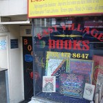 Exterior storefront of East Village Books NYC: shop window with red and yellow signage and books on display.