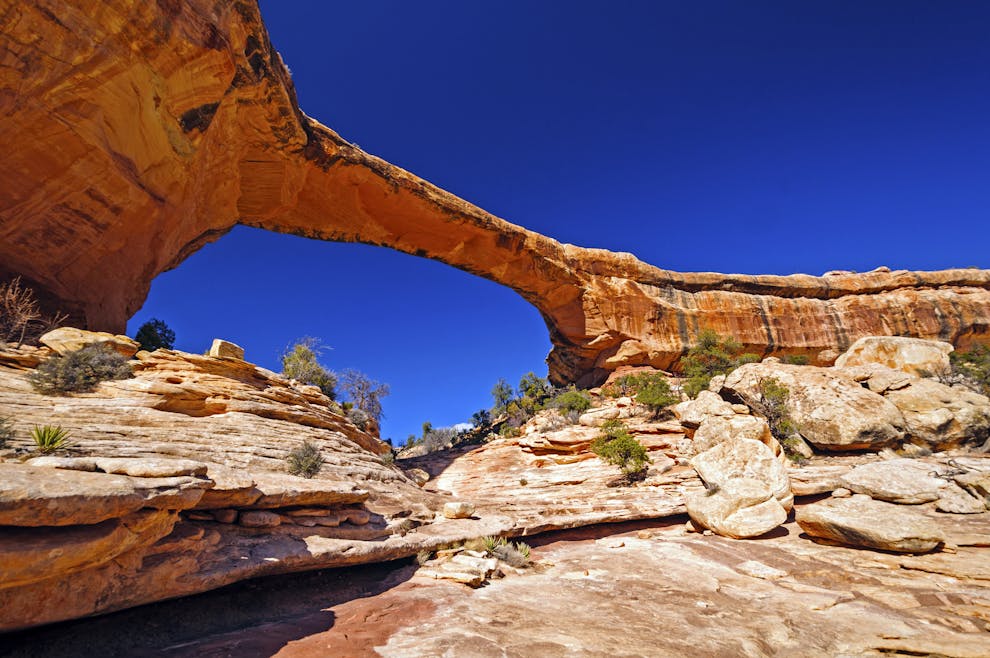 Natural stone arch bridge over a red rock canyon under a deep blue sky