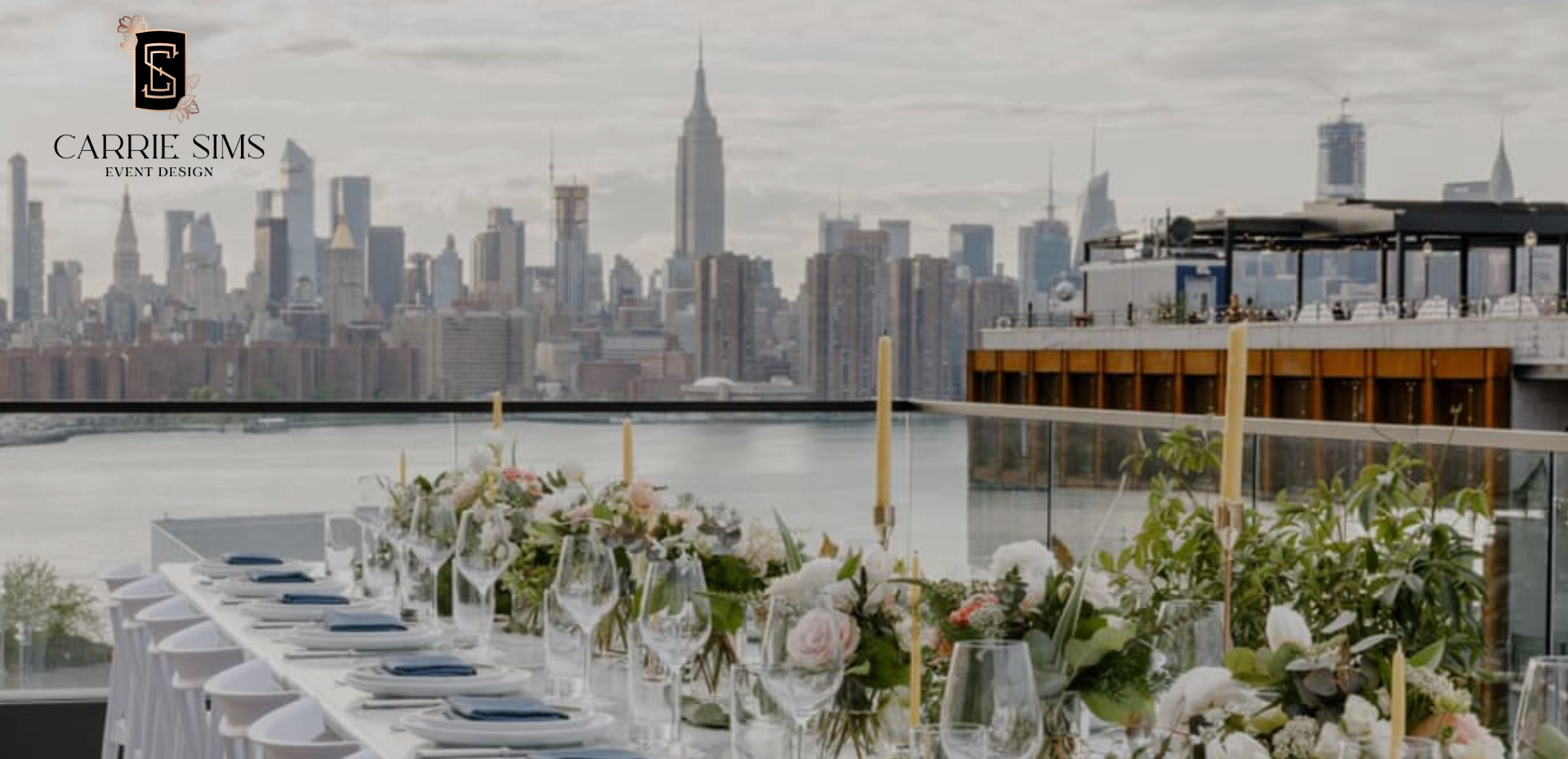 Rooftop dinner table styled with florals, candles and glassware, with the Manhattan skyline and Hudson River behind