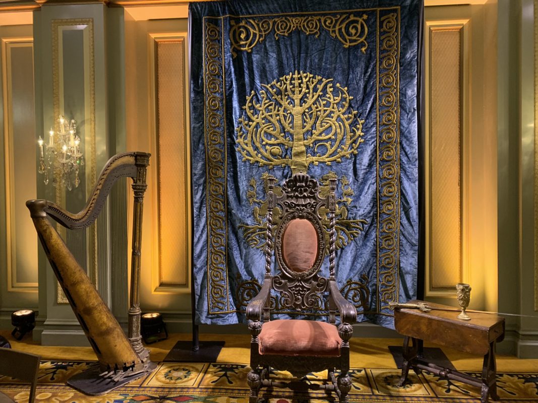 Ornate BYUtv ballroom set with an antique throne, a harp, and an embroidered blue tree tapestry