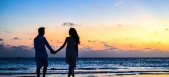 Couple silhouetted holding hands on a beach at sunset
