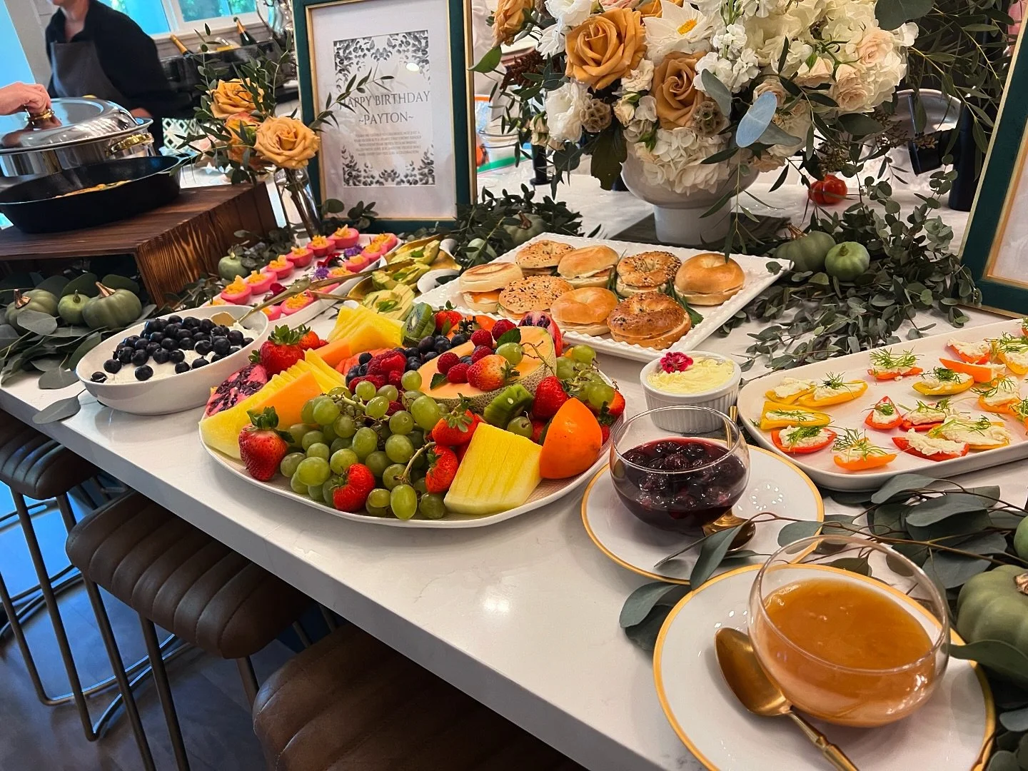 Colorful birthday brunch spread with fruit, bagels and flowers