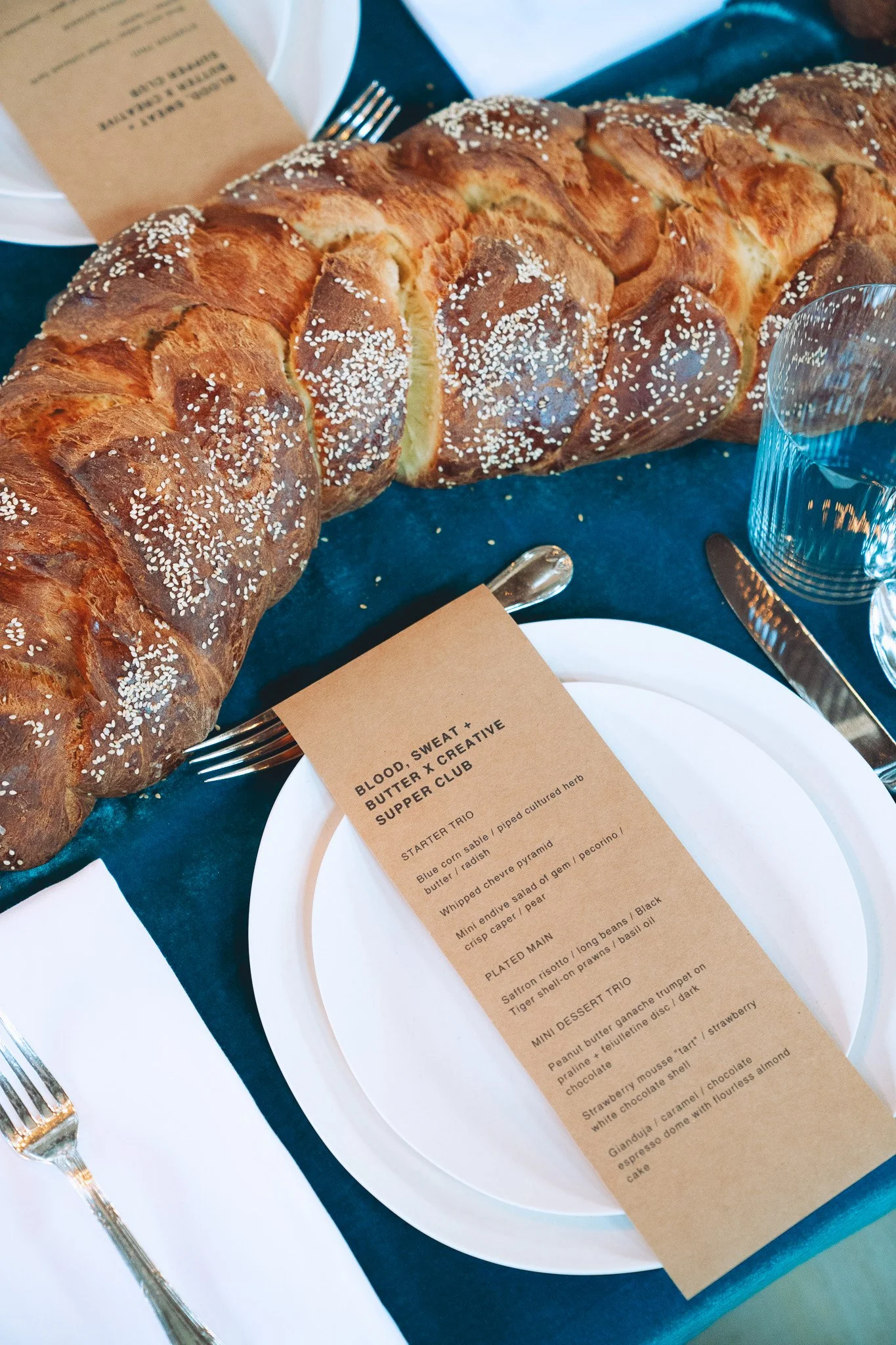 Braided challah and printed menu card on teal velvet