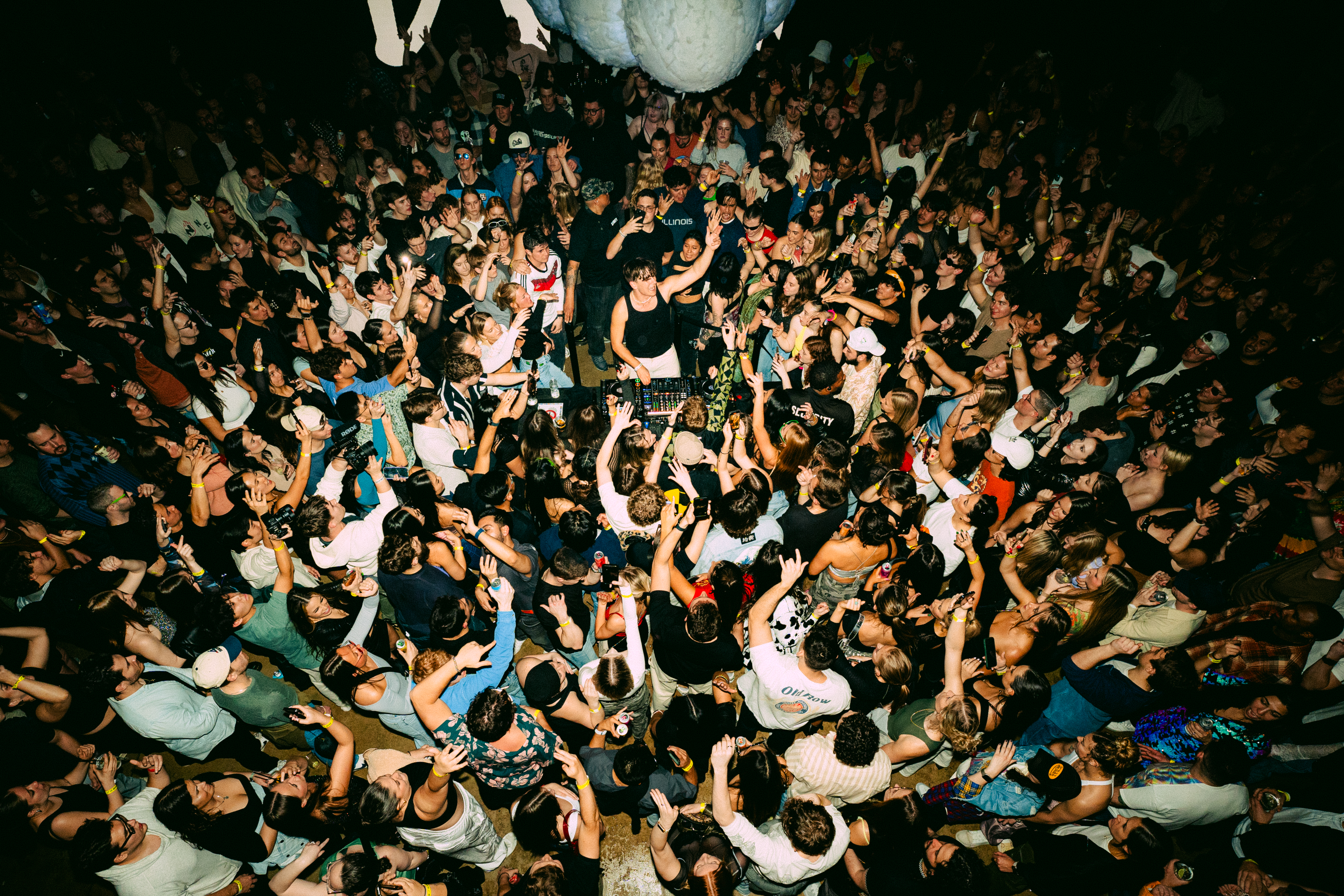 Aerial view of a dense DJ dance crowd with the DJ at turntables in the center