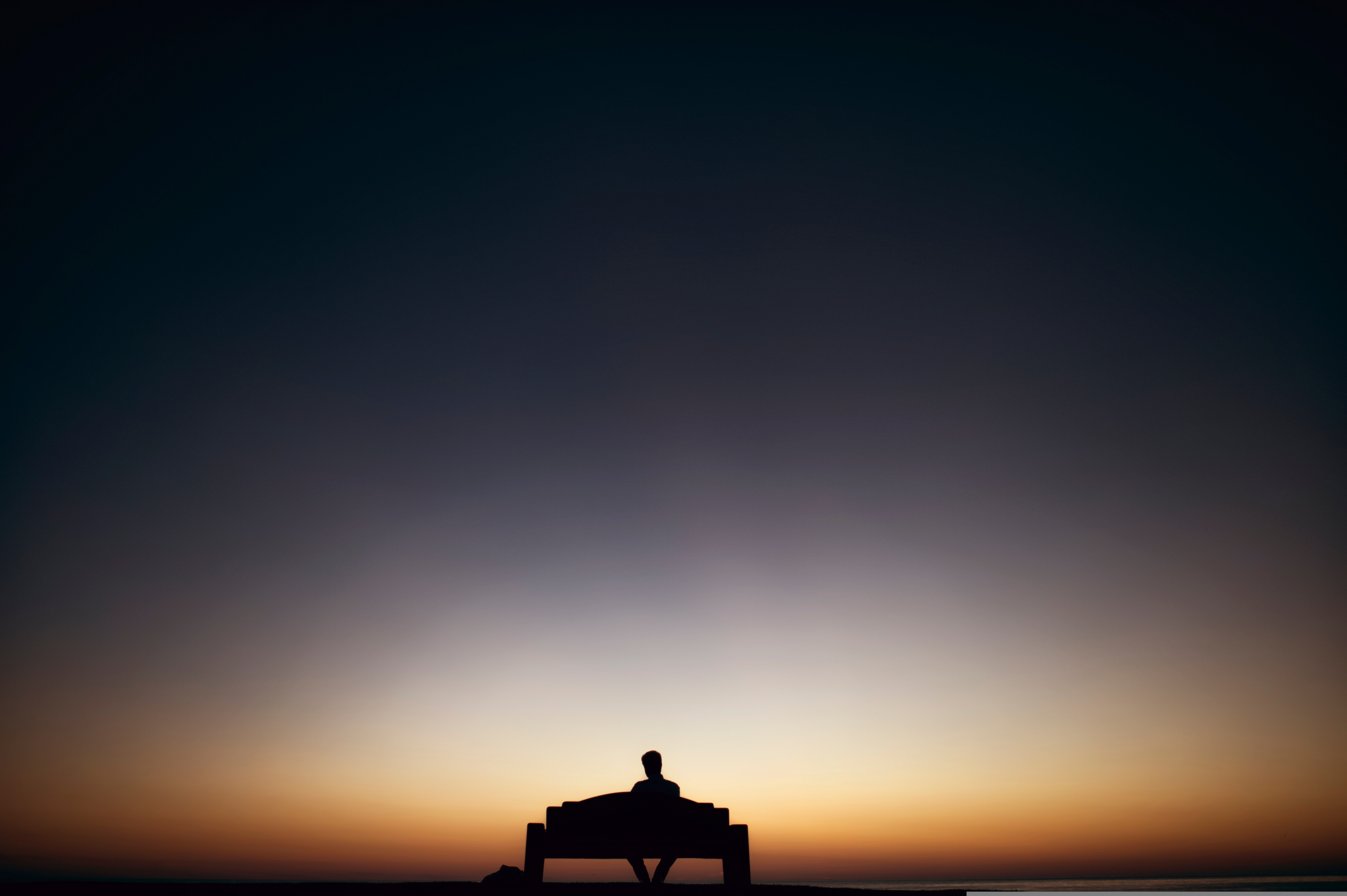 Silhouette of a lone person sitting on a bench at dusk