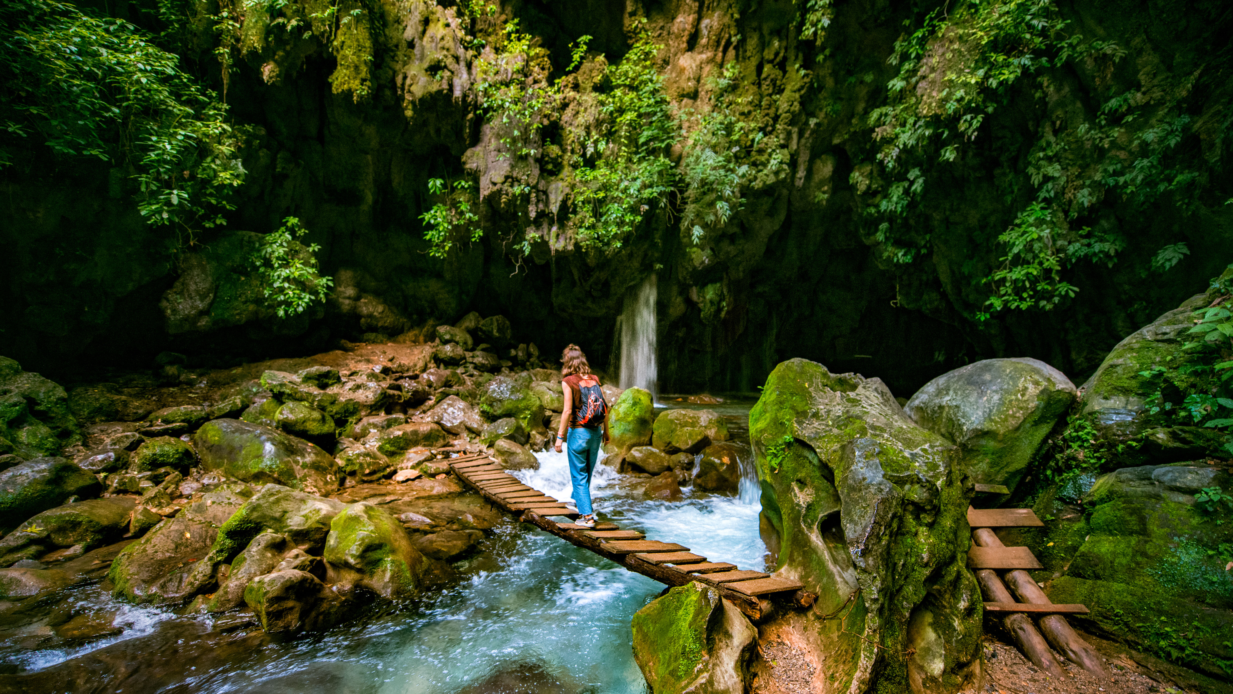 A traveler crossing a wooden bridge over a jungle river — a new way of being