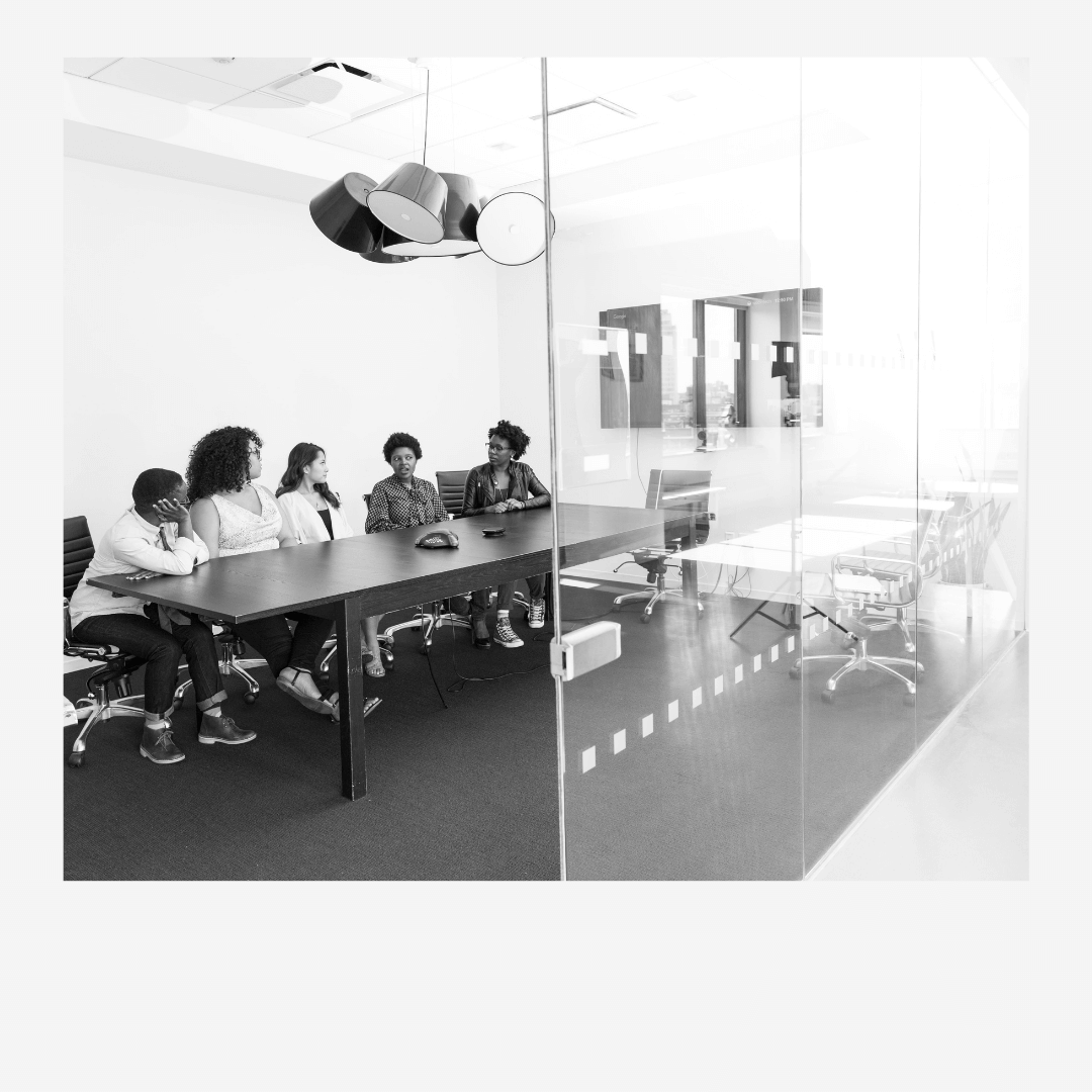 Group of women meeting around a conference table, seen through a glass wall, black and white