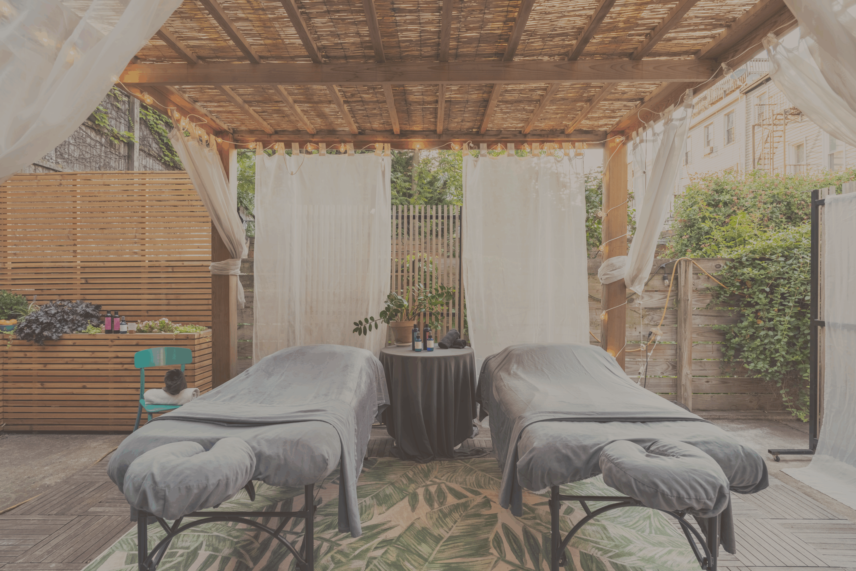 Outdoor pergola spa area with two massage tables, white curtains and a lush garden