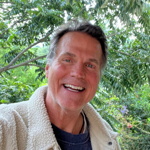 Brit Poulson, PhD, Sr. Leadership Consultant & Coach — grey-haired man smiling outdoors in front of green jungle foliage