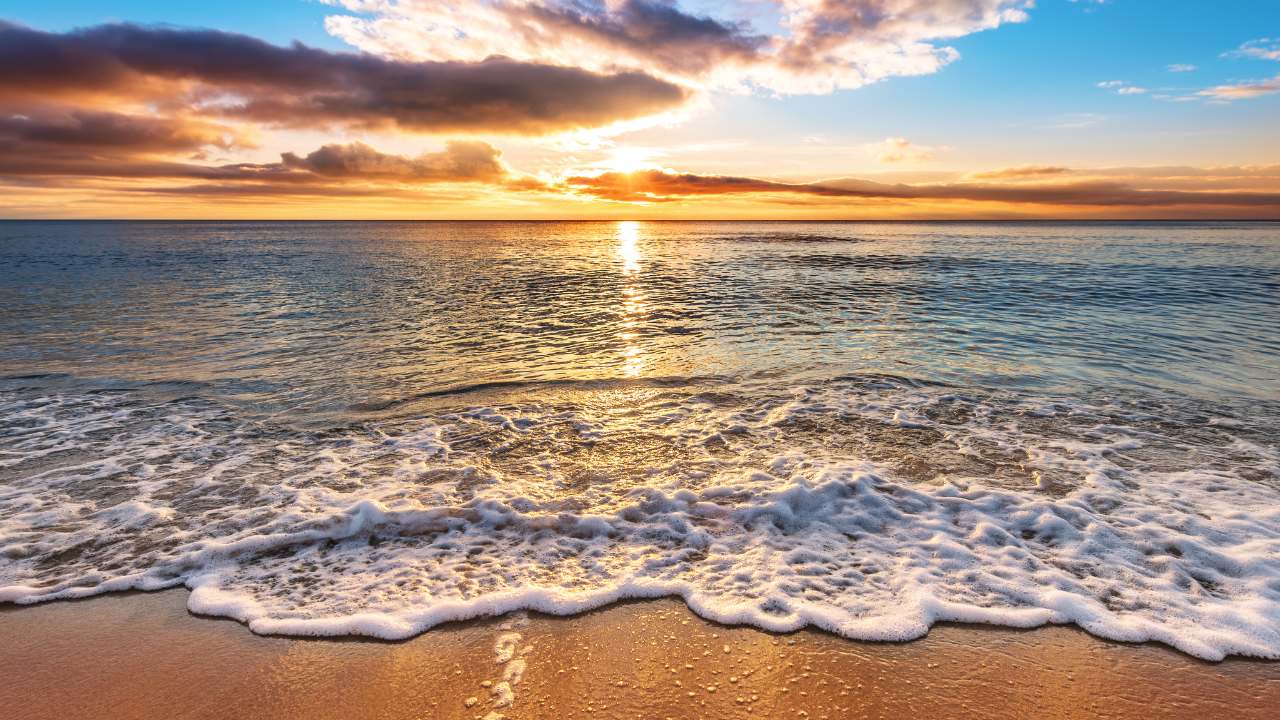 Ocean waves washing onto a sandy shore beneath a golden sunset sky