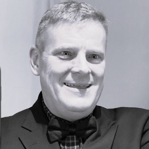 David Forster, Leadership Consultant & Coach — black-and-white portrait of a man in a suit and bow tie, smiling