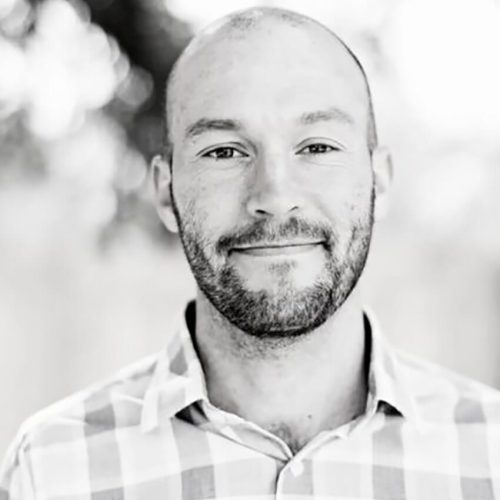 Josh Neil, Sr. Leadership Consultant & Coach — black-and-white portrait of a bald man with stubble in a plaid shirt