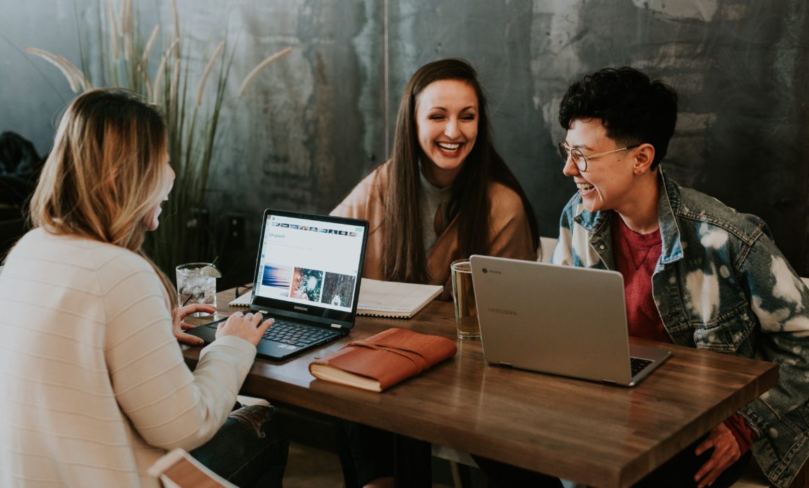 Three young people laughing while working on laptops at a table