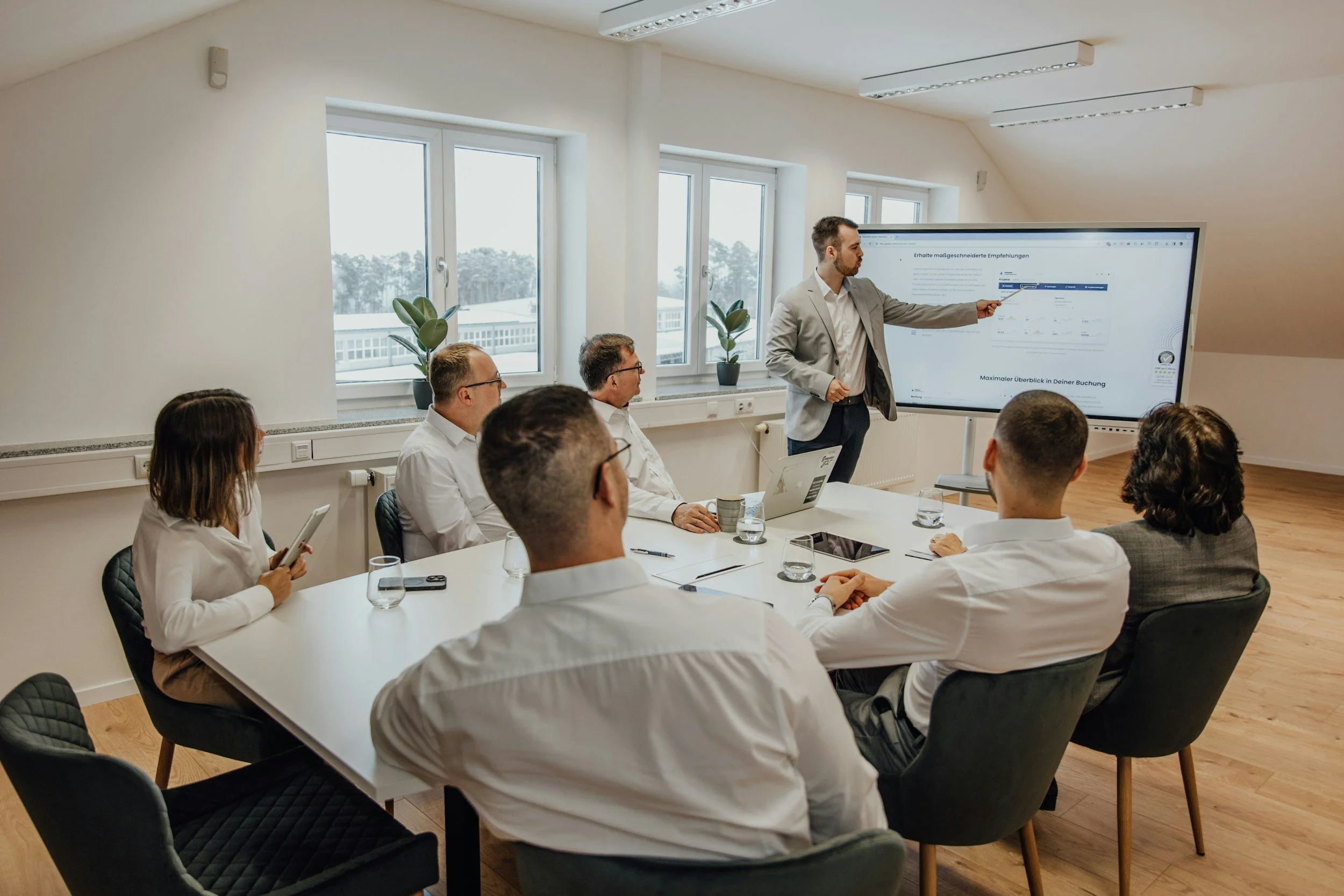 Business team seated at a conference table watching a presenter point at a large display screen.