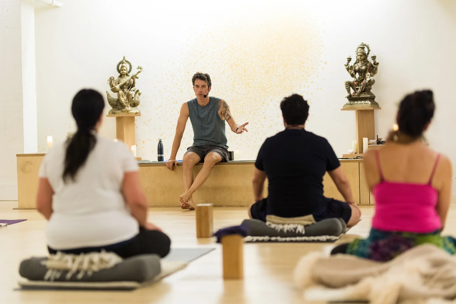 Chad Jayadev Woodford teaching a seated meditation class in front of golden deity statues