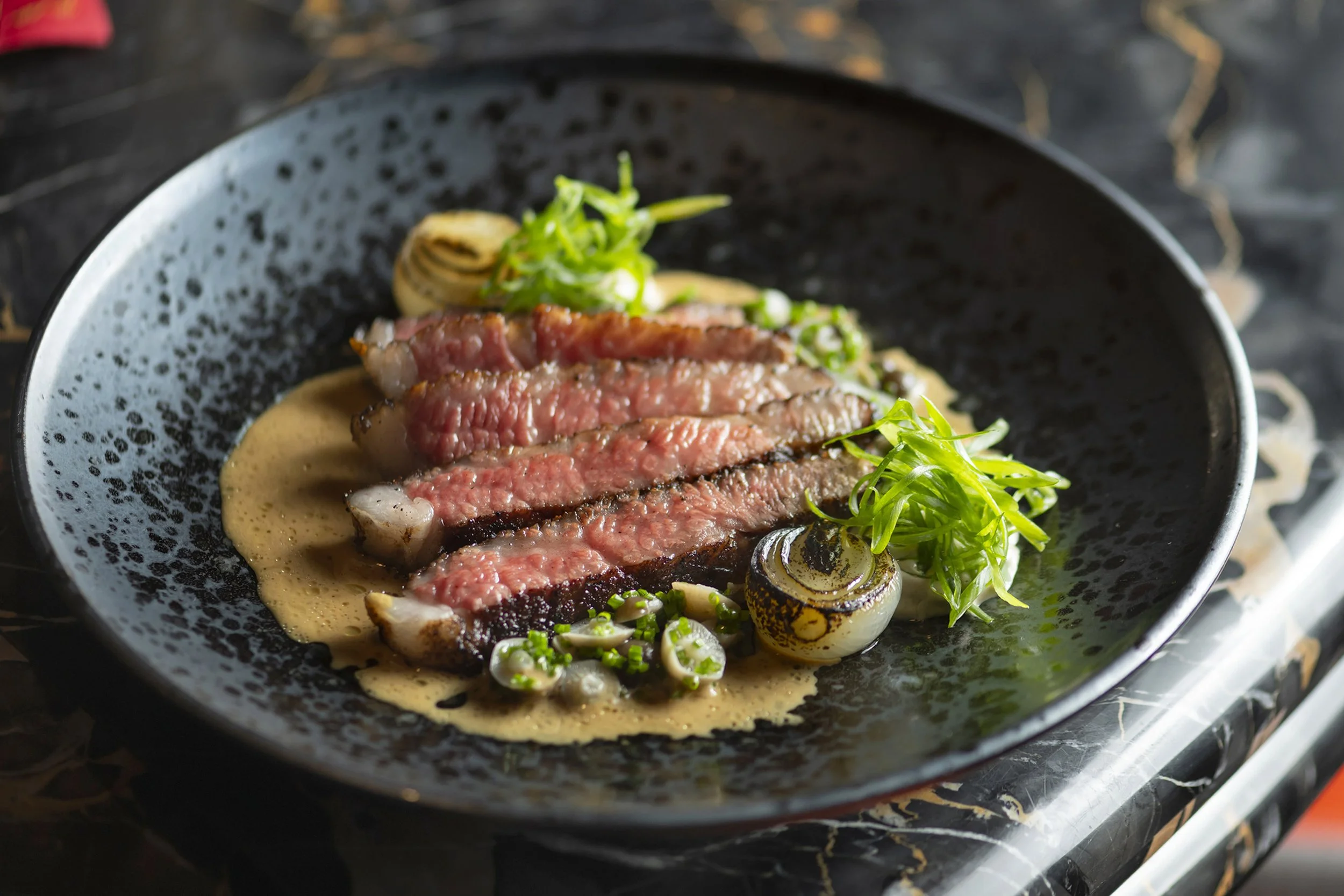 Plated sliced medium-rare steak with mushroom sauce and micro greens, fine dining presentation