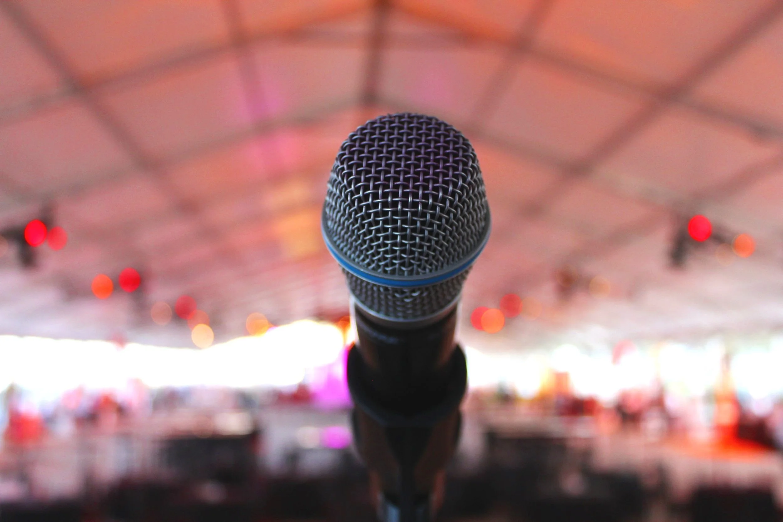 Close-up of a handheld microphone with bokeh lights of an event tent crowd behind it