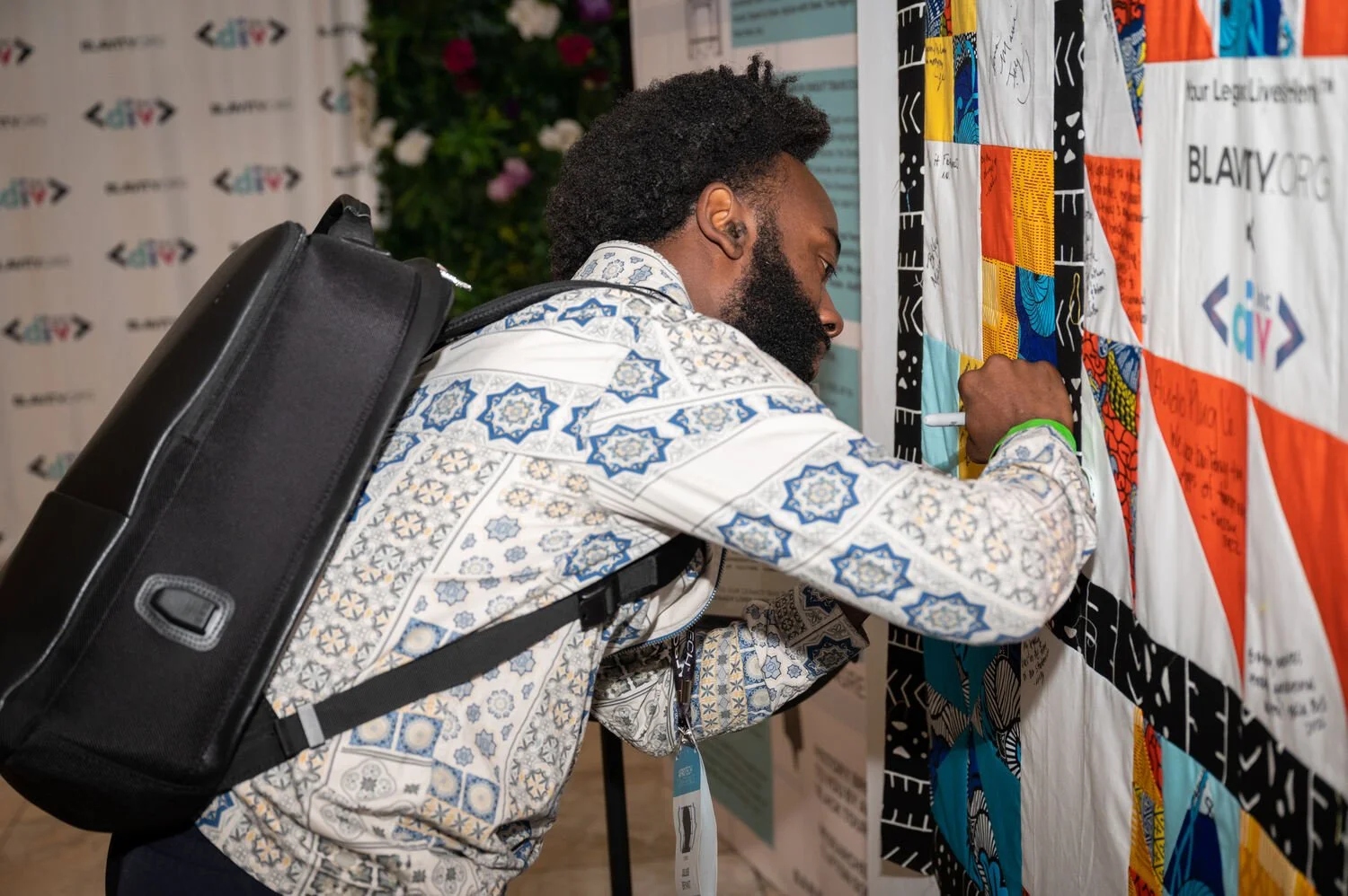 Man signing a colorful quilt installation at a Blavity event