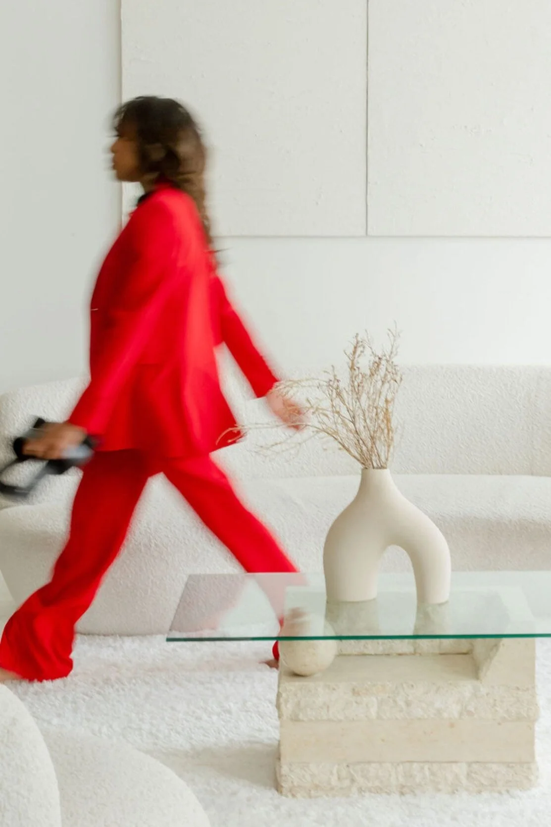 Motion-blurred woman in a red suit walking through a minimalist interior