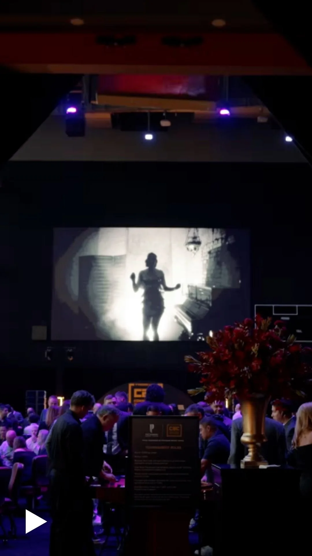 Dark event venue with projection screen and red floral centerpiece