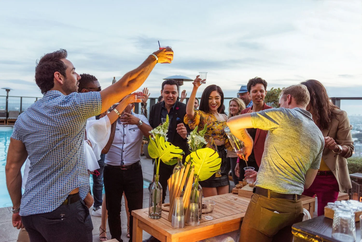 Group of guests toasting drinks at a rooftop event party with tropical florals