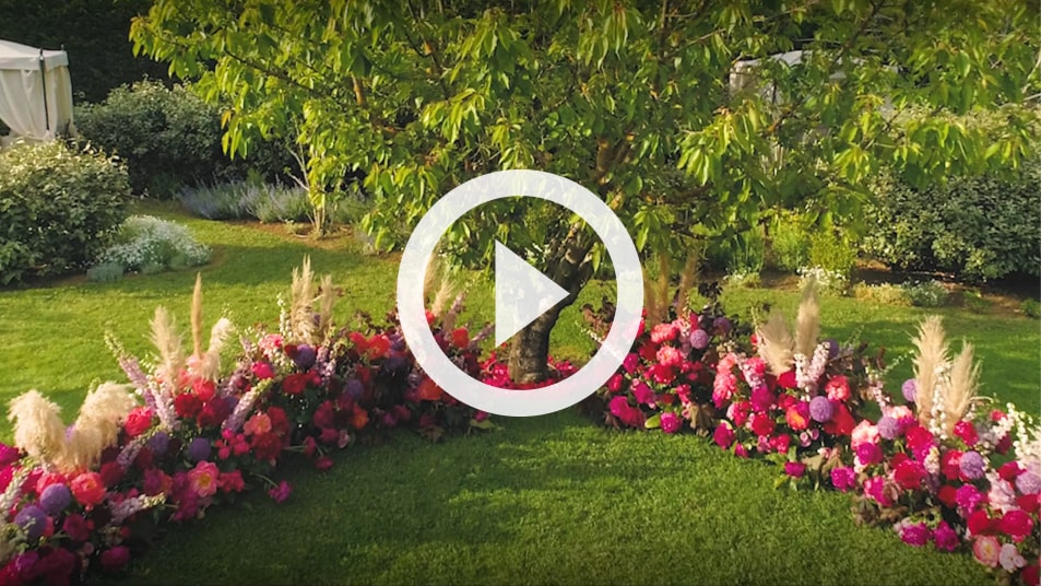 Garden venue with pink and magenta floral ground arrangements around a tree in Tuscany