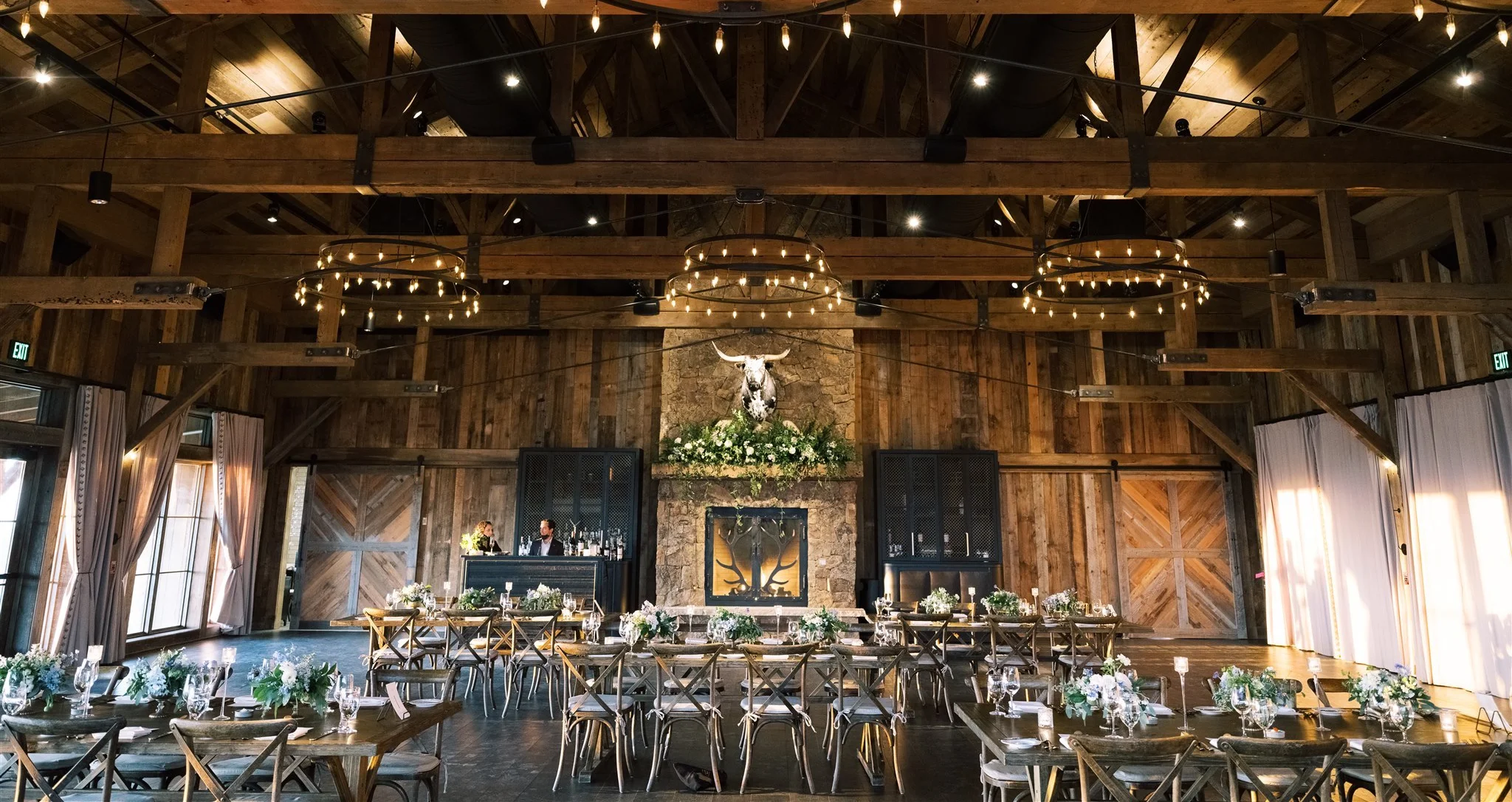 Rustic barn reception hall with Edison bulb chandeliers and wooden beams