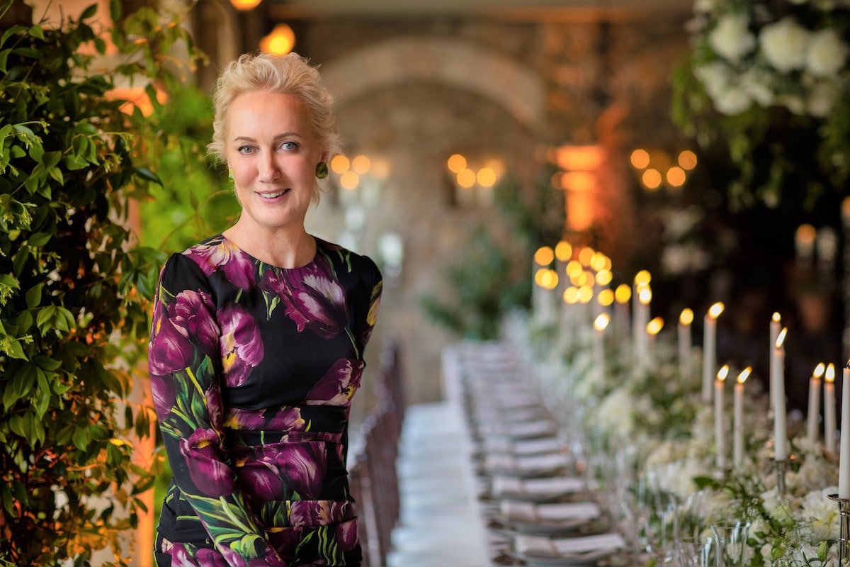 Cristina Verger, a blonde woman in a floral dress, smiling in front of a candlelit banquet hall