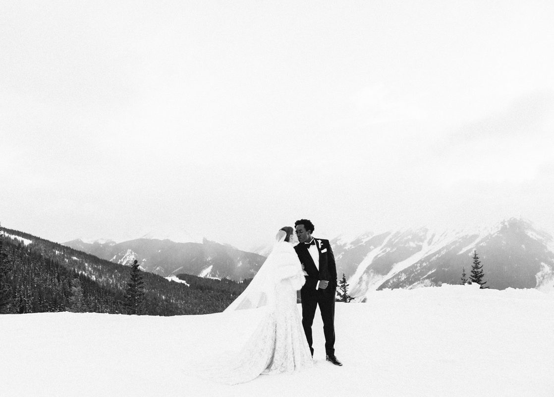 Black and white portrait of a bride and groom embracing in a snowy mountain landscape
