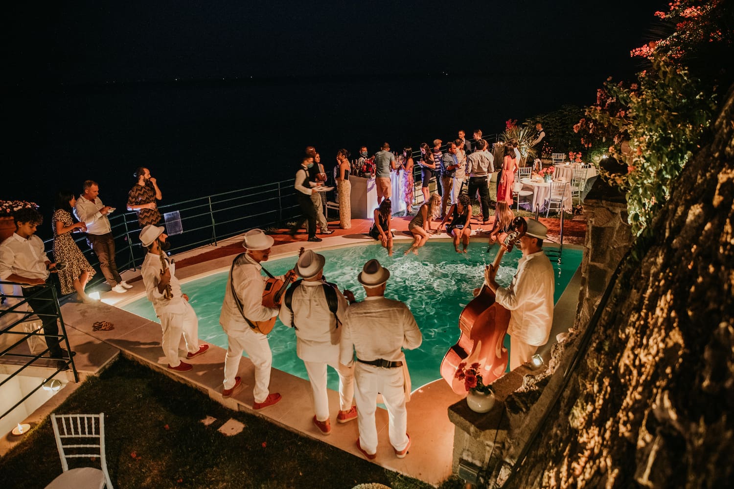 Nighttime outdoor wedding party around a pool with live musicians at an Italian coastal villa