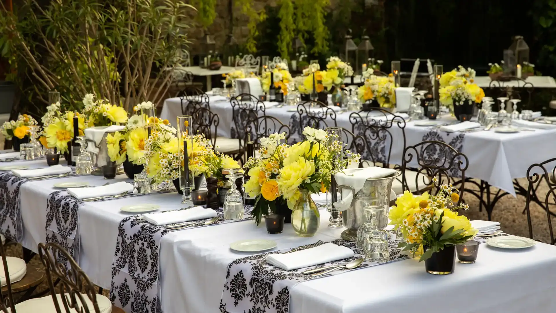 Outdoor garden reception tables with white linens, yellow centerpieces and black damask runners