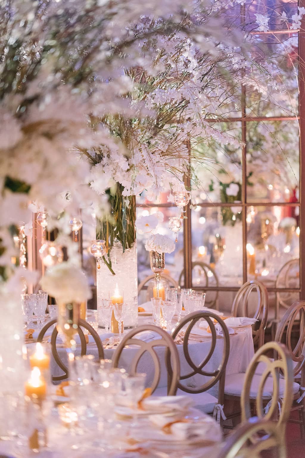 Dreamy white orchid and candlelit reception table detail with a gold mirror-paned backdrop