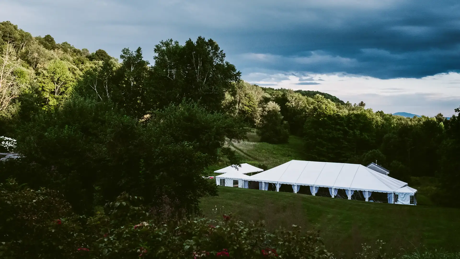 White frame tent in a green hillside landscape under dramatic storm clouds