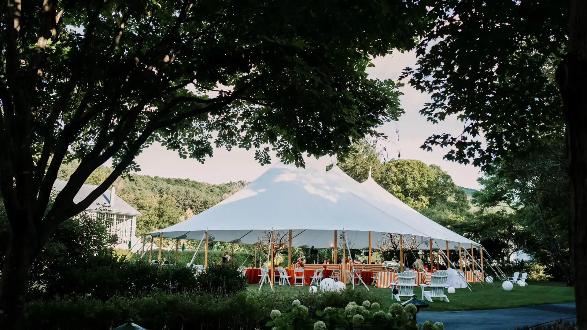 White sailcloth tent reception framed by trees with colorful orange and striped decorations