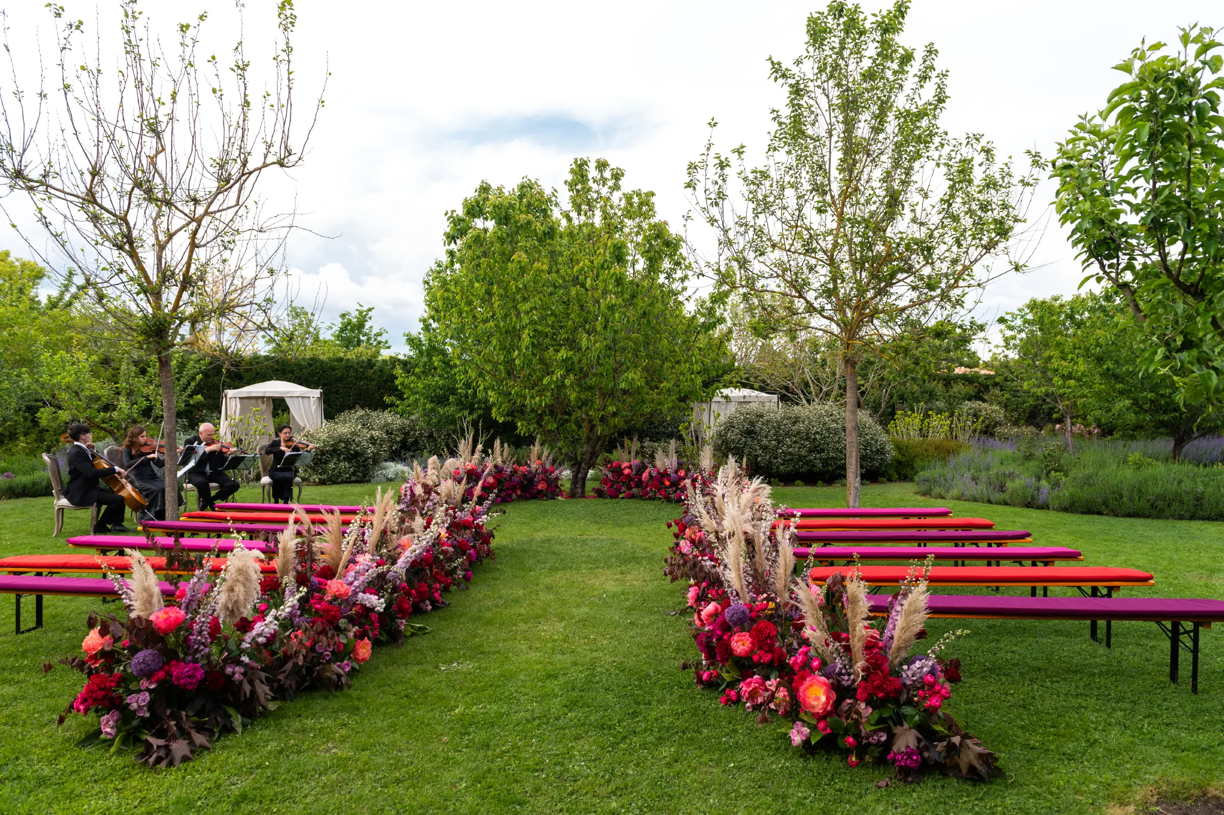 Garden wedding ceremony with vibrant pink and red floral aisle arrangements