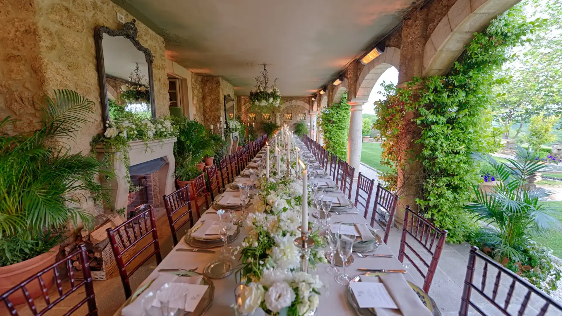 Long banquet table set on a lush ivy-covered stone loggia with white floral centerpieces