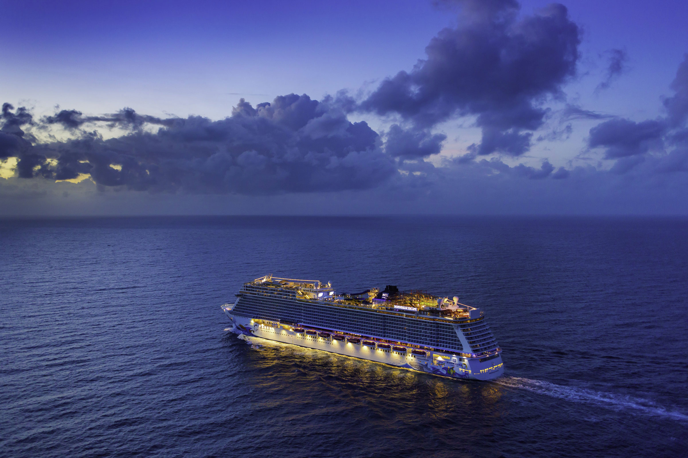 Norwegian Escape cruise ship illuminated at dusk over the open ocean