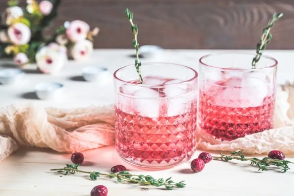 Two pink cranberry cocktails with thyme sprigs in textured glasses
