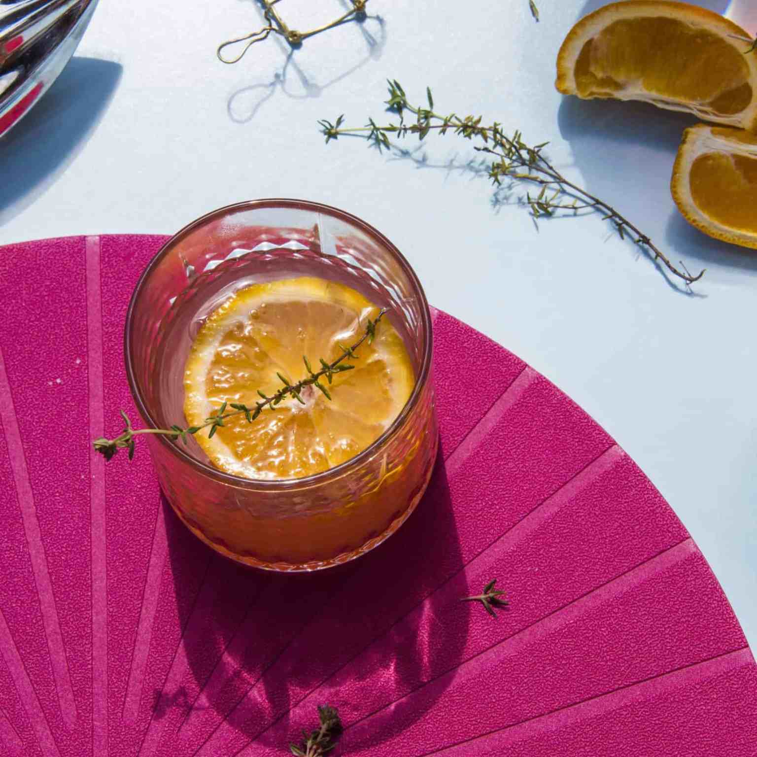 Overhead citrus cocktail with a thyme sprig on a pink fan placemat