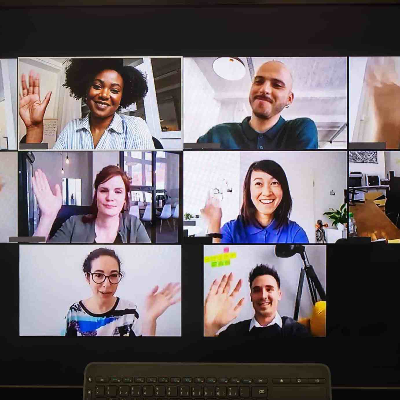 Monitor showing a video call with six participants waving