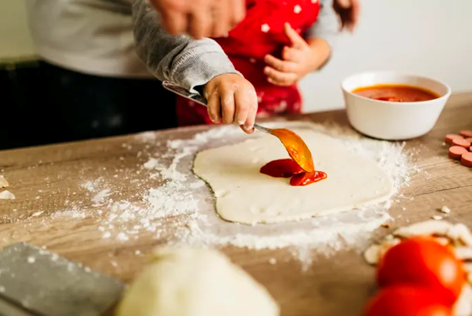 Hands spreading tomato sauce on pizza dough on a floured surface