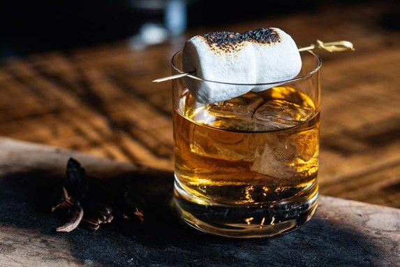Amber whiskey in a rocks glass with a toasted marshmallow on a cocktail pick