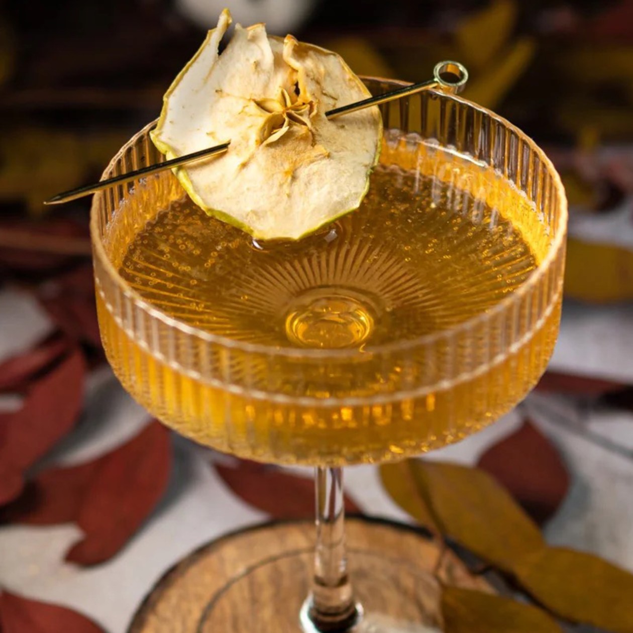 Golden cocktail coupe with a dried apple slice garnish against autumn leaves